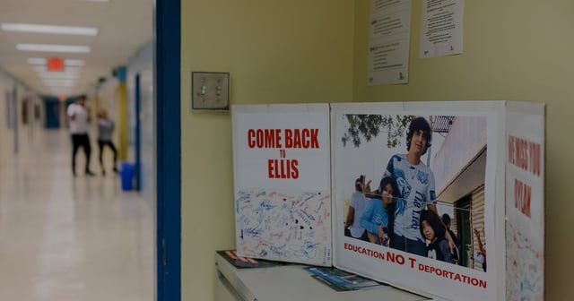 A photograph of a poster board with a portrait of a high school student placed in a hallway.