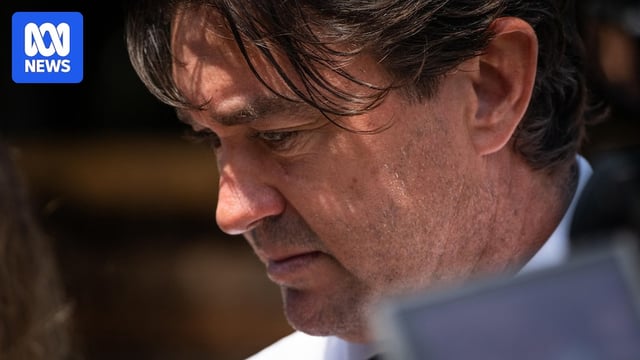 A close-up of a man with dark hair, looking towards the ground.