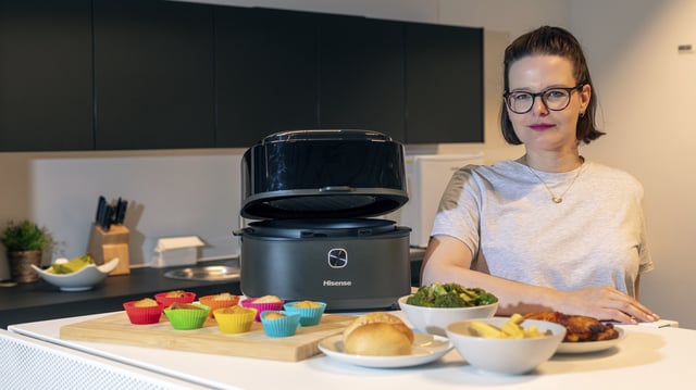 Hisense Airfryer HAF1350DR mit geöffnetem Deckel auf Küchentisch, daneben verschiedene zubereitete Speisen.