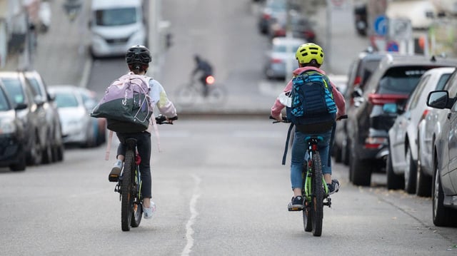Zwei Schulkinder fahren mit ihren Fahrrädern eine Straße entlang.