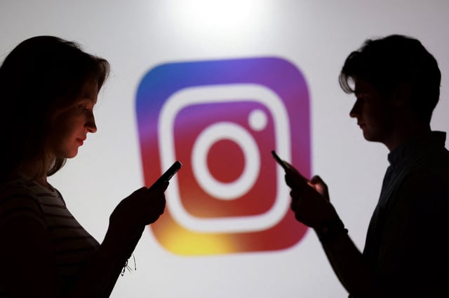 Teenagers pose for a photo while holding smartphones in front of a Instagram logo in this illustration taken September 11, 2025. REUTERS/Dado Ruvic/Illustration/File Photo