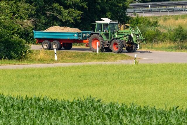 Ein Traktor mit beladenem Anhänger steht an einer Landstraßen-Kreuzung. (Symbolbild)