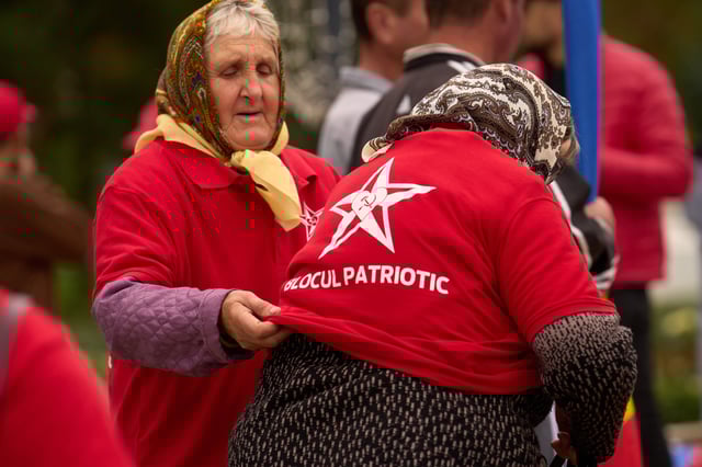 A woman gets help with taking off a red shirt decorated with the hammer and sickle after attending a rally of the Russia-friendly Patriotic Electoral Bloc in Chisinau, Moldova, Thursday, Sept. 25, 2025, ahead of parliamentary elections taking place on Sept. 28. (AP Photo/Vadim Ghirda)