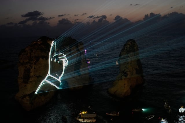 The landmark Raouche sea rock is illuminated by the hand of the late Hezbollah leader Sayyed Hassan Nasrallah during an event commemorating his death in Israeli airstrikes nearly a year ago, in Beirut, Lebanon, Thursday, Sept. 25, 2025. (AP Photo/Hussein Malla)
