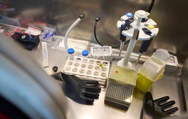 Image of an enclosed metal workspace littered with lab equipment, including tubes, pipettes, and rubber gloves.