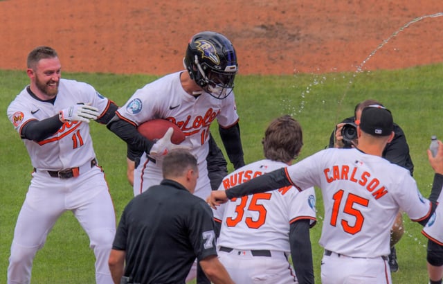 Baltimore Orioles third baseman Jordan Westburg #11 encourages batter Dylan Beavers to run the water gauntlet while donning a Baltimore Ravens helmet and carrying a football as he crosses home plate following his clutch solo home run during the ninth inning of the final home major league baseball game of the season at Oriole Park at Camden Yards. Baltimore came from behind to edge Tampa Bay, 6-5. (Karl Merton Ferron/Staff)