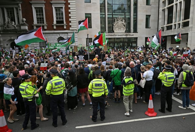 Des policiers encadrent une manifestation de soutien au trio nord-irlandais Kneecap, et à son chanteur Liam O'Hanna alias Mo Chara, où des drapeaux palestiniens sont agités, à Londres le 20 août 2025
