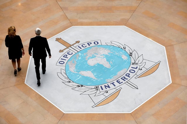 FILE - People walk on the Interpol logo at the international police agency headquarters in Lyon, central France, Nov. 8, 2018. (AP Photo/Laurent Cipriani, File)