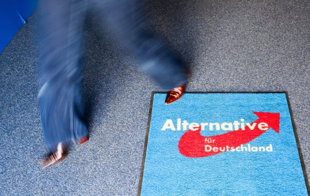 Eine Person mit rotem Schuh läuft über einen blauen Teppich mit dem Logo der AfD. Aufgenommen bei einer Wahlparty in der Bundesgeschäftsstelle der AfD vor der vorgezogenen Bundestagswahl 2025. Frau läuft über AfD-Teppich in der Bundesgeschäftsstelle: Die Partei muß Zentrale 2026 räumen. Foto: picture alliance/dpa | Julian Stratenschulte