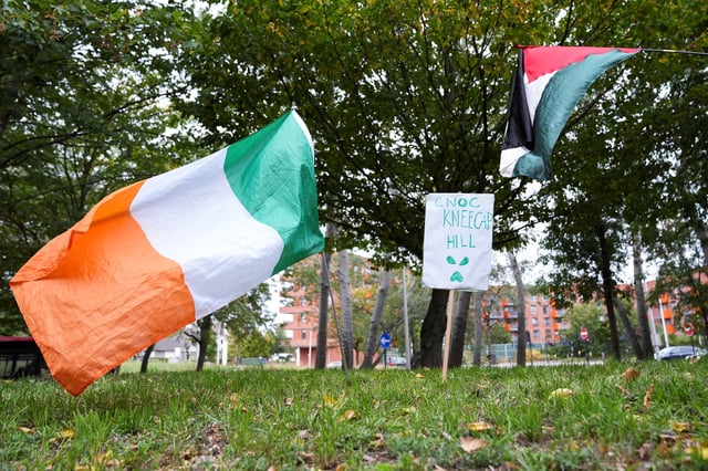 A sign that reads "CNOC Kneecap Hill" is placed next to the Irish and Palestinian flags outside the Woolwich Crown Court on the day Kneecap member Liam O'Hanna, also known as Liam Og O hAnnaidh and performing under the name of Mo Chara, who has been charged with a terrorism offence in relation to the alleged display of a Hezbollah flag onstage in 2024, appears in court, in London, Britain, September 26, 2025. REUTERS/Maja Smiejkowska