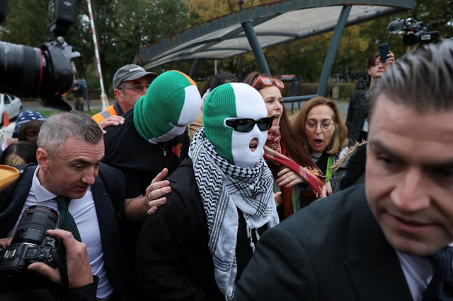 Member of the rap group Kneecap, Liam O'Hanna, also known as Liam Og O hAnnaidh and performing under the name of Mo Chara, who has been charged with a terrorism offence in relation to the alleged display of a Hezbollah flag onstage in 2024, wears a keffiyeh and a balaclava in the colours of the Irish flag, as he walks outside the Woolwich Crown Court on the day of a hearing, in London, Britain, September 26, 2025. REUTERS/Hannah McKay