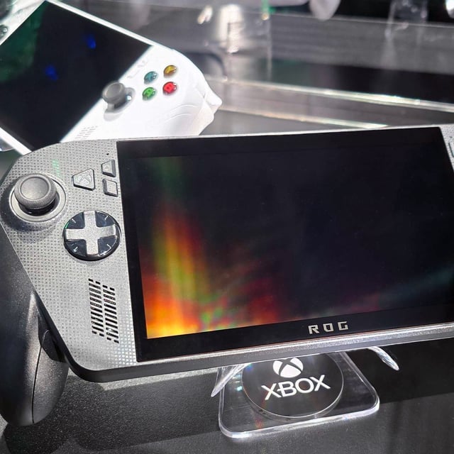 ASUS ROG Xbox Ally X (black) and ROG Xbox Ally (white) in a glass display case at Gamescom in August, 2025.