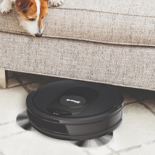 A jack russell looking at the Shark AV2501S AI Ultra Robot Vacuum clean under the couch.