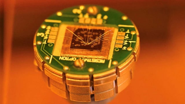 The researchers used a novel material in tiny memory devices, here seen as clusters of golden dots on the top of the chip.