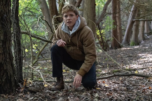 Mae Martin kneeling in a forest.