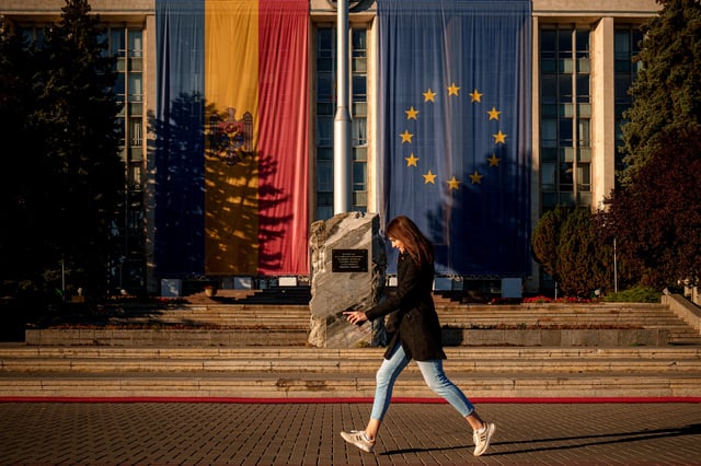 A woman runs in front of the government building, decorated with European Union and Moldovan flags in Chisinau, Moldova, Friday, Sept. 26, 2025, ahead of parliamentary elections taking place on Sept. 28. (AP Photo/Vadim Ghirda)