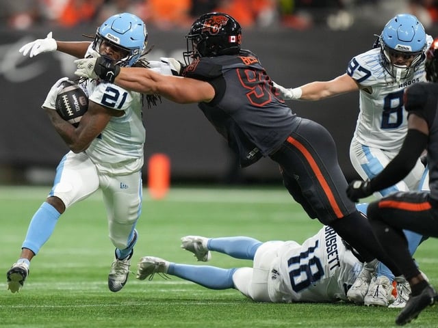 Toronto Argonauts' Spencer Brown carries the ball as B.C. Lions' Levi Bell  reaches to tackle him during CFL game, in Vancouver, on Friday, September 26, 2025.
