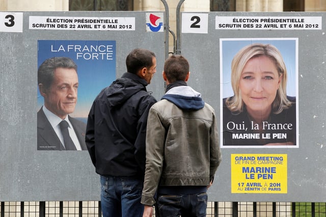 People stop to read the official campaign posters for candidates in the French presidential election: Nicolas Sarkozy, France's President and UMP candidate and Marine Le Pen, France's National Front head in Paris, April 9, 2012. REUTERS/Benoit Tessier/File Photo