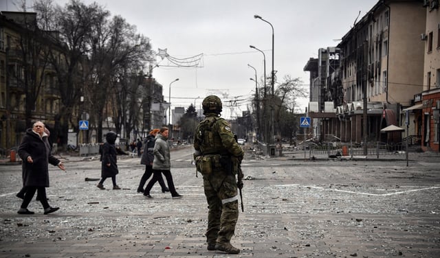 La gente pasa junto a un soldado ruso en el centro de Mariupol el 12 de abril de 2022, mientras las tropas rusas intensifican una campaña para tomar la ciudad portuaria estratégica, parte de un ataque masivo anticipado en el este de Ucrania, mientras el presidente de Rusia presenta un caso desafiante para la guerra contra Rusia. vecino. - *NOTA DEL EDITOR: Esta foto fue tomada durante un viaje organizado por el ejército ruso.* (Foto de Alexander NEMENOV / AFP)