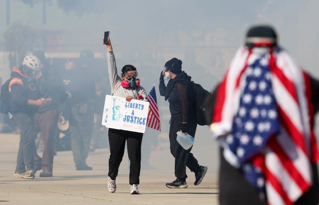 A protester holds up her phone and backs away from federal agents shooting chemical gas at protesters along Harvard Street near the U.S. Immigration & Customs Enforcement facility on Sept. 26, 2025, in Broadview. Federal agents used several kinds of chemical gasses, baton rounds, and arrested at least two people while protesters refused to clear the street. (Stacey Wescott/Chicago Tribune)