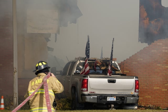 A vehicle that was rammed into the building is surrounded by smoke as a firefighter works on the scene at the Church of Jesus Christ of Latter-day Saints in Grand Blanc, Mich., Sunday, Sept. 28, 2025.