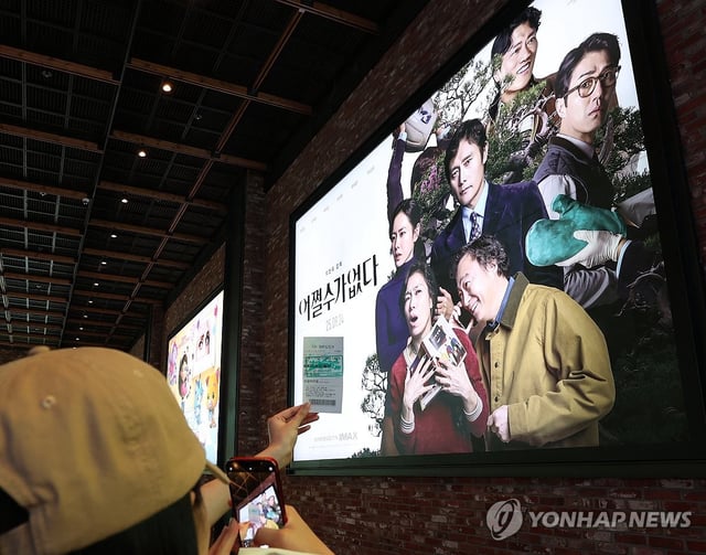 A moviegoer takes a photo of their ticket with a "No Other Choice" poster in the background at a Seoul cinema on Sept. 25, 2025. (Yonhap) 