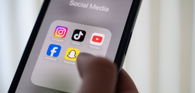 Jemand hält ein Smartphone, auf dessen Display verschiedene Social Media Apps angezeigt werden