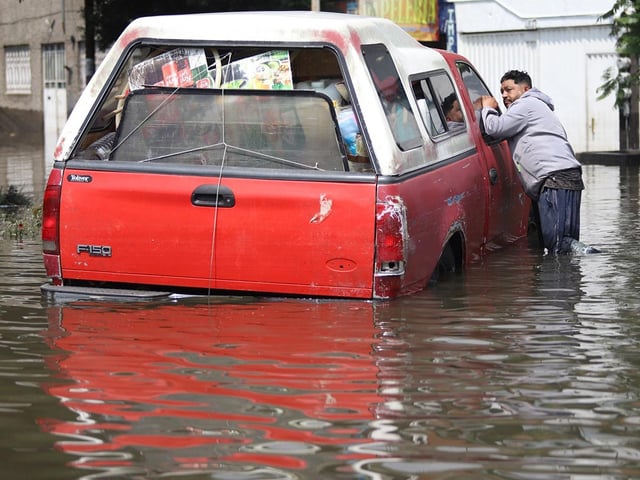 Un señor parado junto a una camioneta en calles inundadas de Iztapalapa