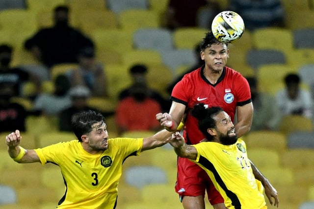 Singapore's Irfan Fandi (back) heads the ball against Malaysia's Facundo Garces (L) and La'Vere Lawrence Corbin-Ong