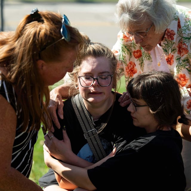 Joanne Green of Fenton, 75, top right, and McKenna Harrington of Davison, 25, second from right, comfort Katelyn Kruse of Fenton, 26, center, after Kruse was present at the scene of a shooting and structure fire at The Church of Jesus Christ of Latter-day Saints on McCandlish Road in Grand Blanc, Mich., Sunday, Sept. 28, 2025. (Katy Kildee/Detroit News via AP)