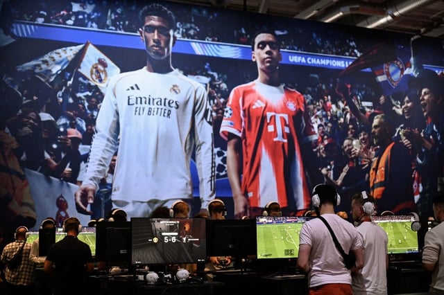 Gamers play the video game "EA Sports FC 26 in front of a screen featuring English midfielder Jude Bellingham (L) and Bayern Munich's German midfielder Jamal Musiala during the Gamescom video games trade fair at the Trade Fair Center in Cologne, western Germany, on the first day of the fair on August 20, 2025. The 2025 edition of the vast Gamescom trade fair in Cologne, Germany, had its opening night on August 19, 2025 and will be running from August 20 to 24, 2025. (Photo by INA FASSBENDER / AFP)
