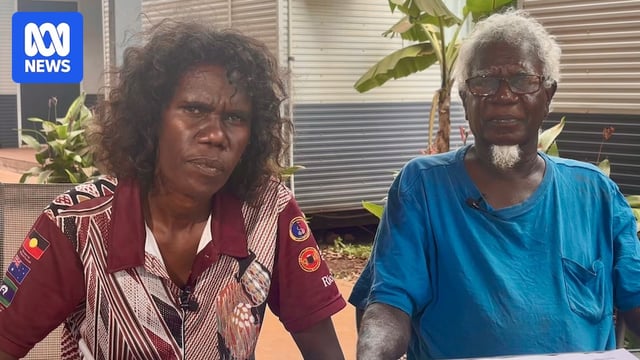 A woman and elderly man sitting at a table with serious expressions.