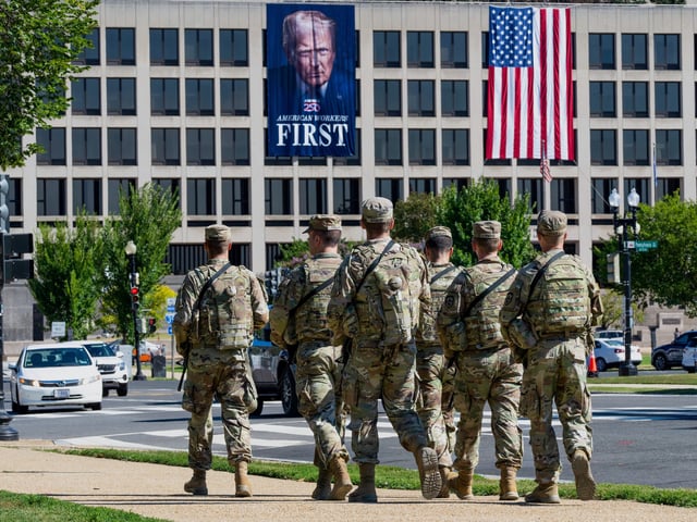 Armed National Guard soldiers from West Virginia patrol the Mall near the Labor Department in Washington, where a poster of President Donald Trump is displayed, Tuesday, Aug. 26, 2025. (AP Photo/J. Scott Applewhite)