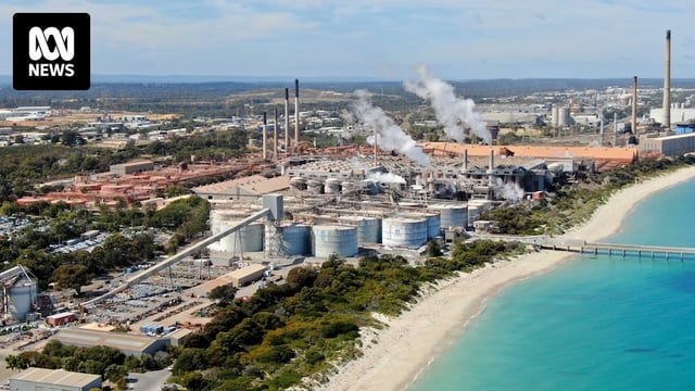 An empty beach leads to a heavy industrial area with large smoke plumes