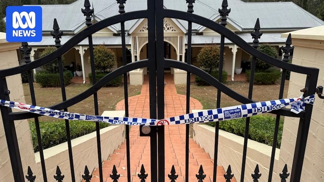 A large black gate at the front of a house with police tape hanging from it.