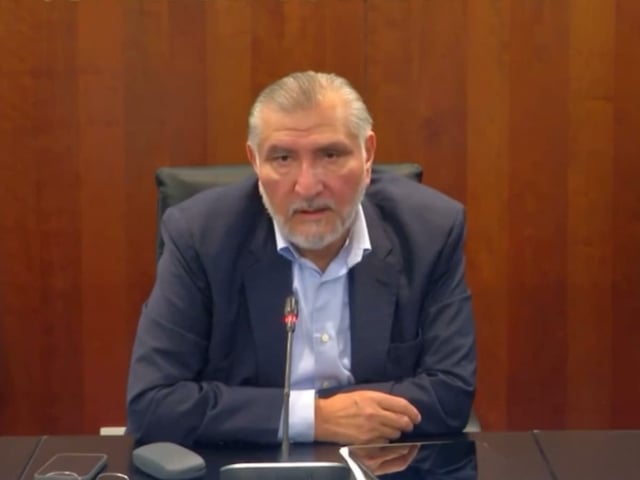 Adán Augusto López Hernández, coordinador de los senadores de Morena, habla en conferencia de prensa desde el Senado de la República, sentado frente a un micrófono con expresión seria y vistiendo saco azul y camisa clara, en un fondo de madera institucional.