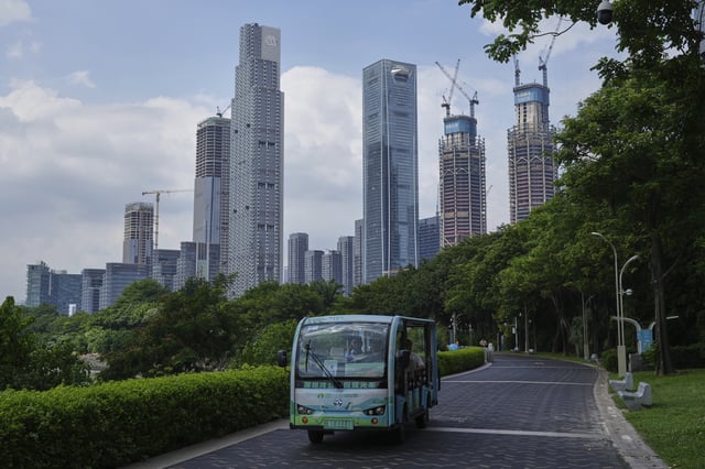 Visitors take a cart tour at a public park along the Shenzhen Bay against the high-rise office buildings, some of which are under construction, in Shenzhen, China's Guangdong province, Wednesday, Sept. 17, 2025. (AP Photo/Andy Wong)