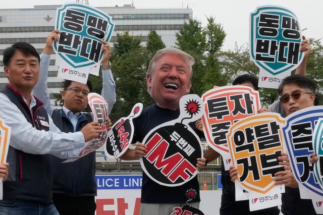 A member of the Korean Confederation of Trade Unions, wearing masks of U.S. President Donald Trump, protests against Trump's tariff policy on South Korea near the presidential office in Seoul, Tuesday, Sept. 30, 2025. The signs read "Stop investment and Oppose alliance?" (AP Photo/Ahn Young-joon)