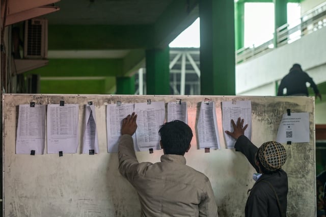 Des proches consultent une liste de noms alors que les opérations de secours se poursuivent à l'école Al-Khoziny à Sidoarjo, en Indonésie, le 30 septembre 2025