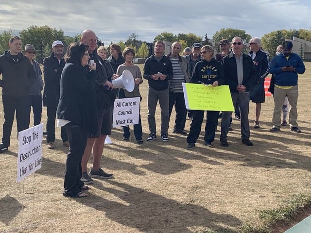 Protesters hold placards at a neighbourhood rally at Herb Link Park in Edmonton on Saturday, Sept. 27, 2025.