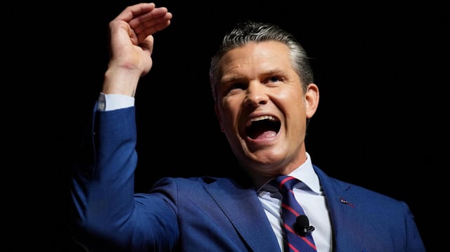 Pete Hegseth spricht mit erhobener Hand.