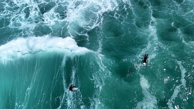 Dieses Luftbild zeigt Surfer, die auf ihren Surfbrettern an den Wellen des Atlantischen Ozeans in Carcans im Südwesten Frankreichs vorbeischwimmen.