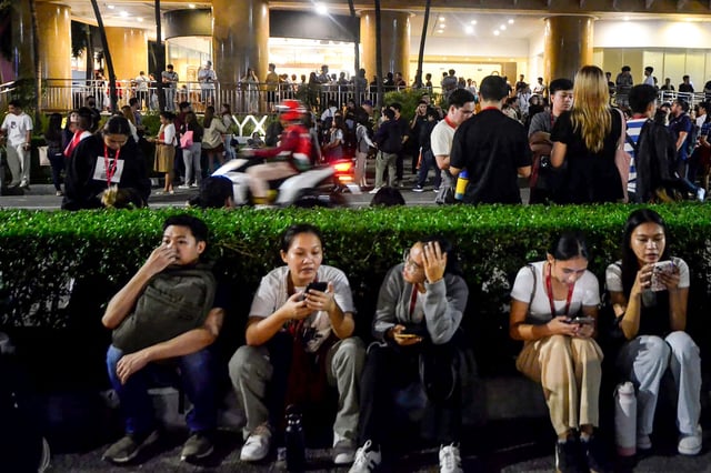 Call center employees surf mobile phones as they gather outside their office building after earthquake tremors at Cebu in central Philippines on September 30, 2025.