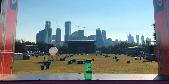 A photo showing an Austin HSEM water bottle in front of the ACL festival with the Austin skyline in the background.