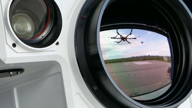 Eine Drohne und eine Abfangdrohne spiegeln sich in der Linse eines mobilen Detektionssystems zur Drohnenabwehr.