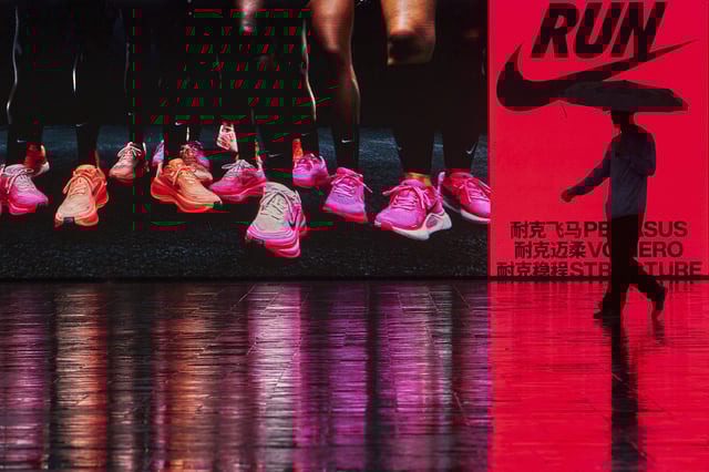 A man holding an umbrella walks by a Nike store advertisement billboard during a rainy day, in Beijing, on August 27, 2025.