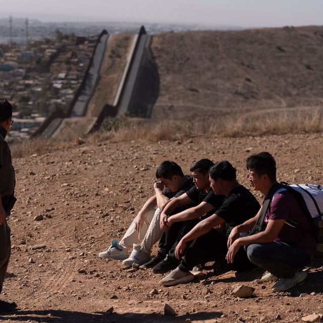 FILE - A U.S. Border Patrol agent walks past four men being detained after crossing the border through a gap in the walls separating Mexico and the United States, Jan. 23, 2025, in San Diego. (AP Photo/Gregory Bull, File)