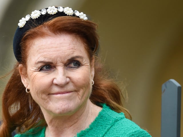 Sarah Ferguson wearing a green jacket and black headband looking to the side and smirking