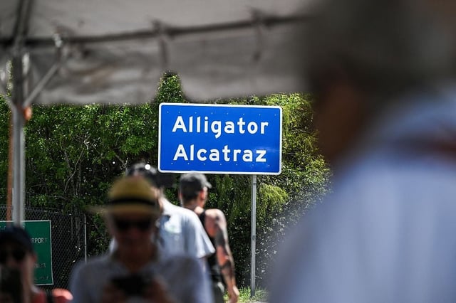 People around an Alligator Alcatraz sign are blurred out while the sign remains in focus.