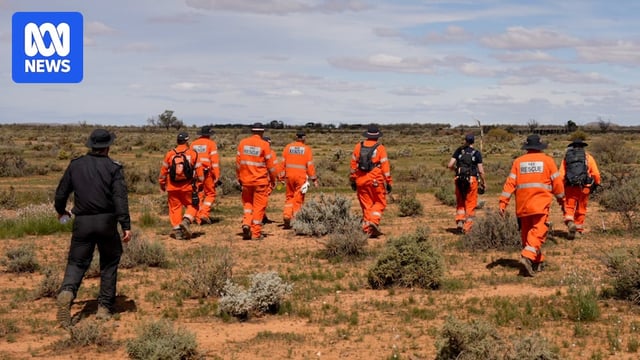 a group of people walk in rugged bushland, they wear orange uniform and police uniform